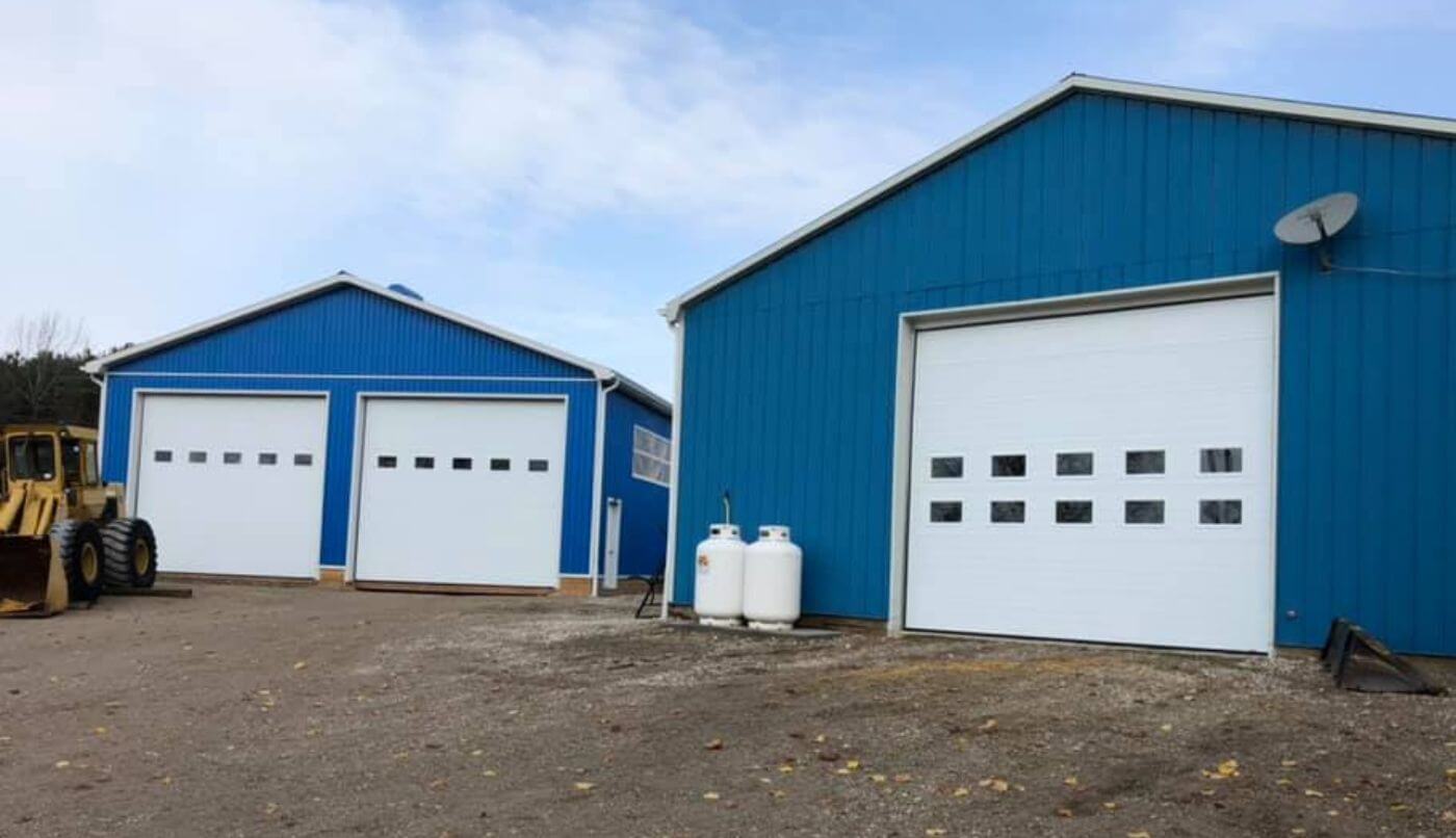 Two blue buildings featuring Ice White doors and windows stand side by side against a clear sky.